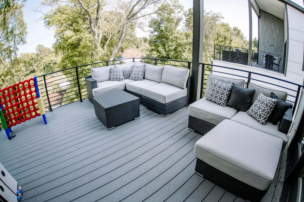 This exterior image showcases a spacious wooden deck with comfortable outdoor seating, decorative cushions, a game table, and lush greenery in the background. The deck is lit by a warm sunset, creating a relaxed and inviting atmosphere ideal for gatherings.