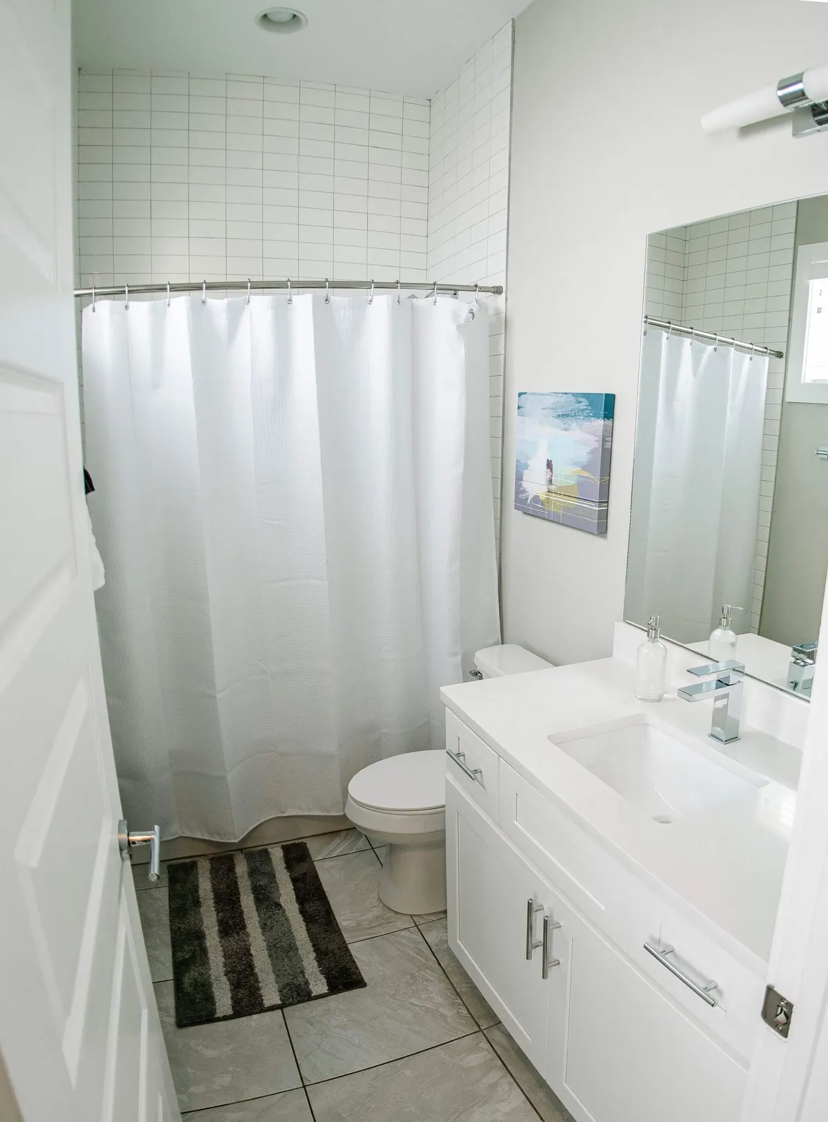 A calming bathroom featuring a vanity with sink, large mirror, shower curtain, and tasteful artwork on the wall. The soft lighting and clean design invite relaxation and make everyday routines a pleasure.