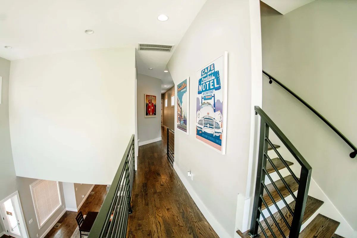 A central stairway and hallway lined with unique artwork and warm wooden floors, leading toward the entry/exit. The space feels open and communal, inviting guests to gather before heading out.