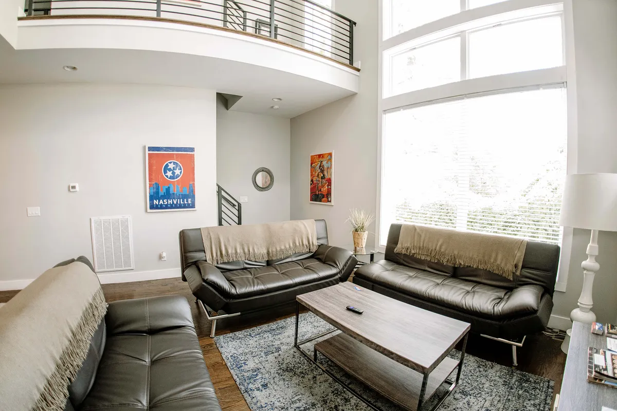 This image showcases a lively living space with comfortable leather sofas, a wooden coffee table, a colorful Nashville poster, and vibrant wall art. The layout exudes a modern and cozy vibe, ideal for group gatherings and celebrations.