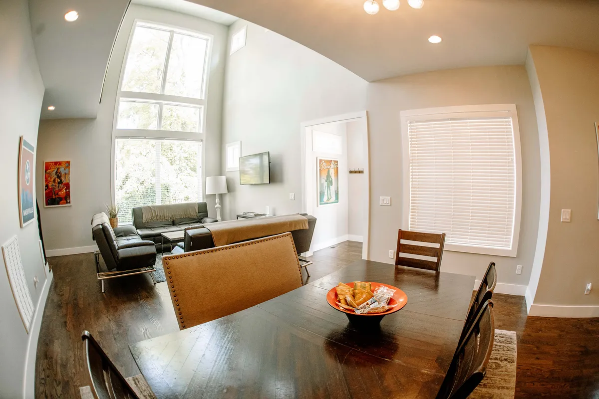 A bright, welcoming family room featuring a modern sofa, a large dining table with a fruit bowl, and expansive windows that let in plenty of natural light. The scene is arranged for family gatherings, casual dining, and relaxing together after a day of exploring.