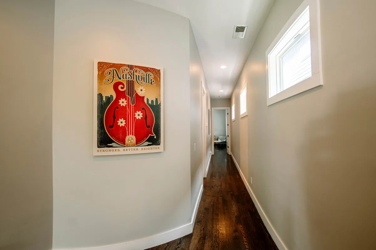 A hallway featuring Nashville-themed artwork and sleek wooden flooring, creating a subtle yet strong sense of place. The space feels inviting and gives guests a tangible connection to the local culture as they move through the home.