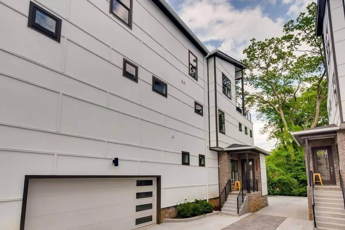 A bright exterior shot featuring modern townhouse architecture framed by lush greenery. The clean, well-maintained look of the building and surrounding area signals a welcoming and safe neighborhood, ideal for evening strolls with pets.