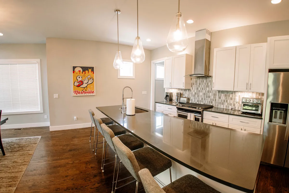A modern kitchen with a prominent island, stylish pendant lights, and artistic touches on the walls. The setting is welcoming and designed for both cooking and entertaining, with ample space for group activities.