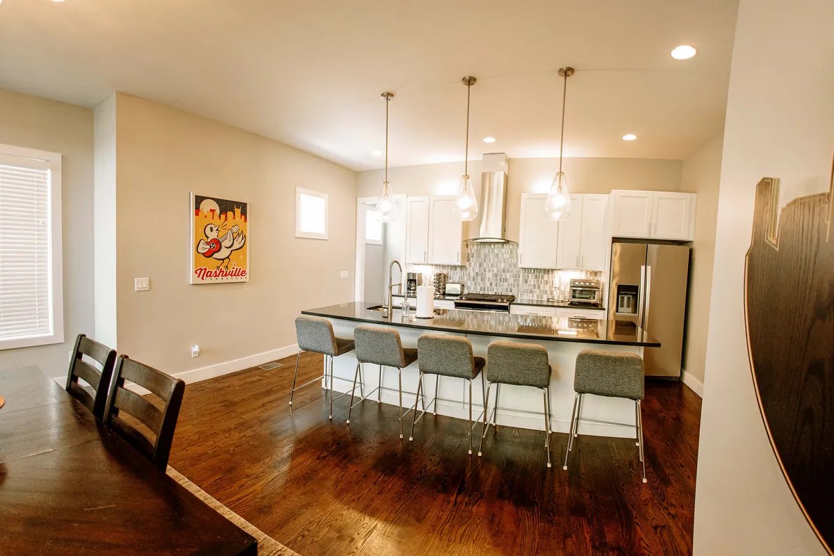 A modern kitchen with a spacious island, sleek pendant lights, stainless steel appliances, and cheerful artwork. The layout encourages group cooking sessions, family breakfasts, and shared culinary experiences before heading out for the day.