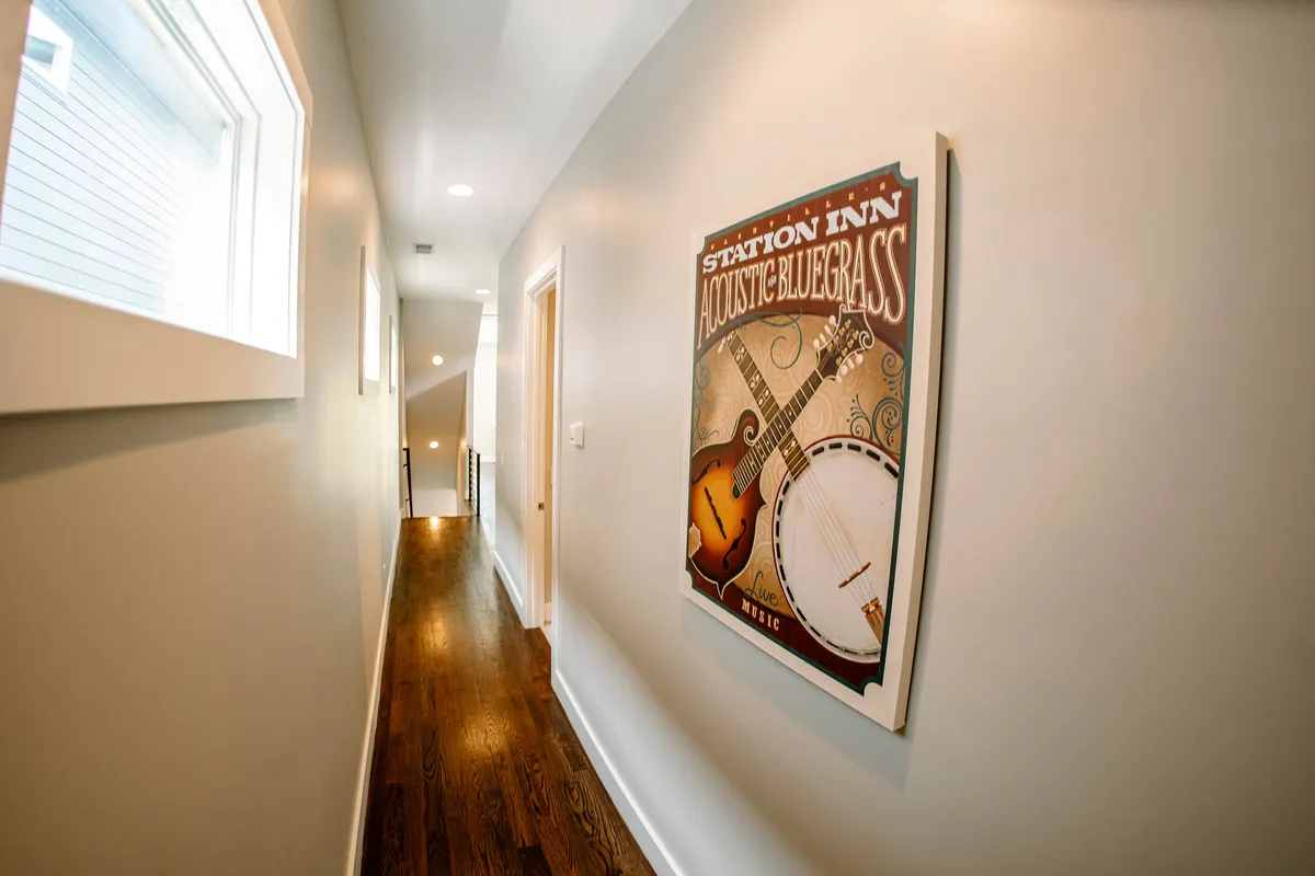 A sunlit hallway with wooden flooring, vibrant musical poster, and large windows allowing plenty of natural light to stream in. The space feels open and welcoming, suggesting easy access and a connection to the outdoors.